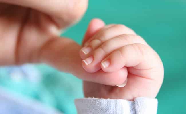 Mão de bebê segurando dedo de um adulto