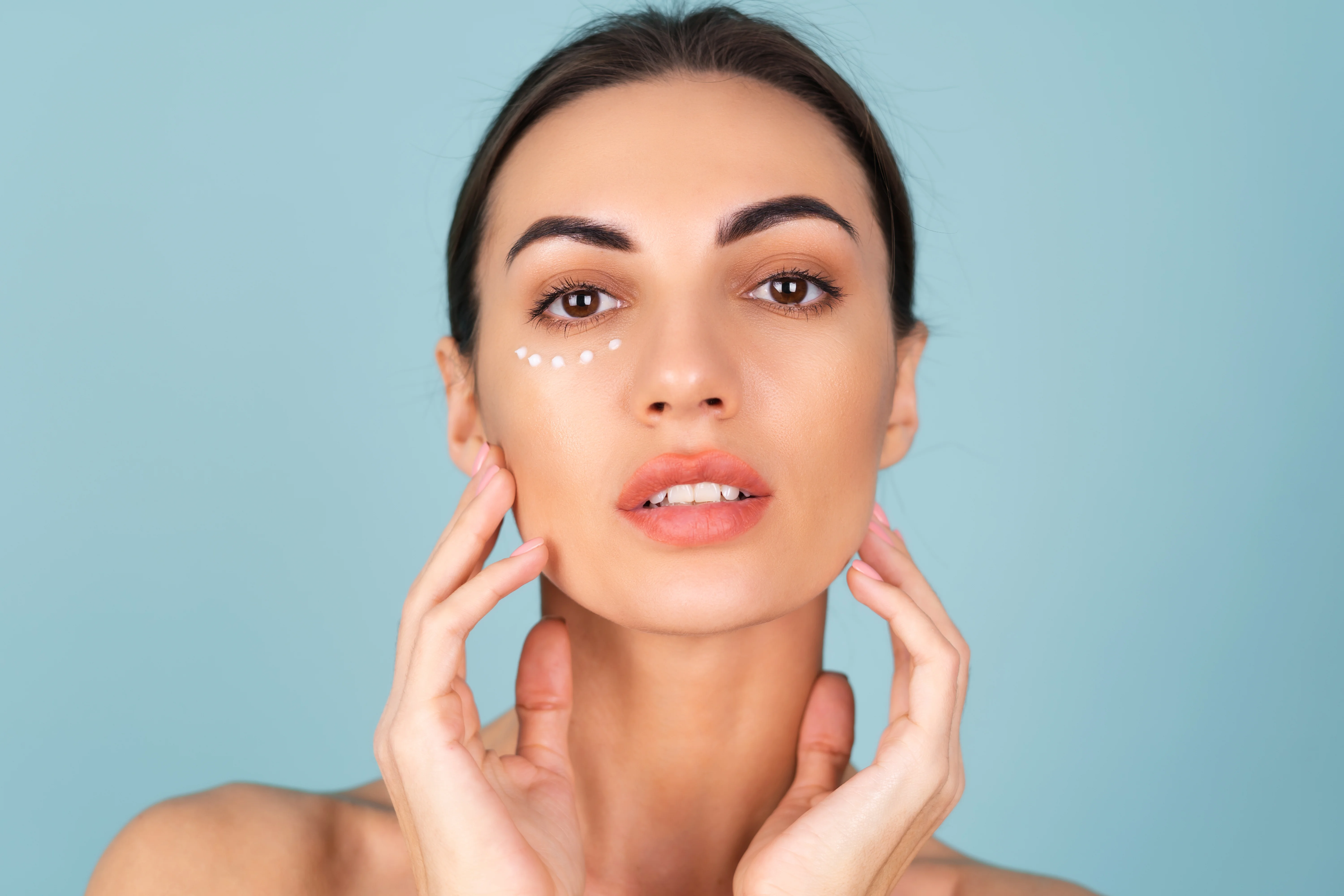 Retrato de beleza de close-up de uma mulher com pele perfeita e maquiagem natural, com pontos de creme antienvelhecimento para hidratar e firmar a pele sob os olhos